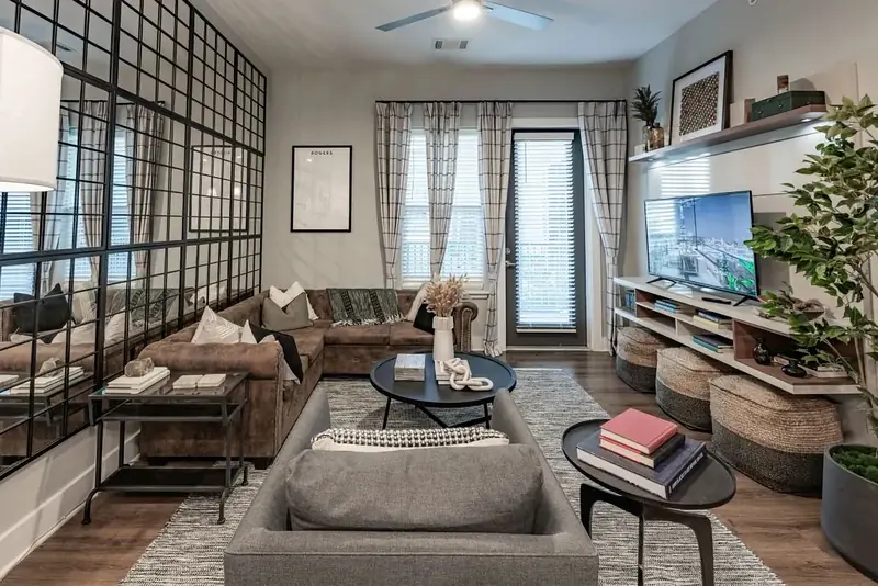 Model apartment living room with sectional sofa, balcony door and black grid glass wall